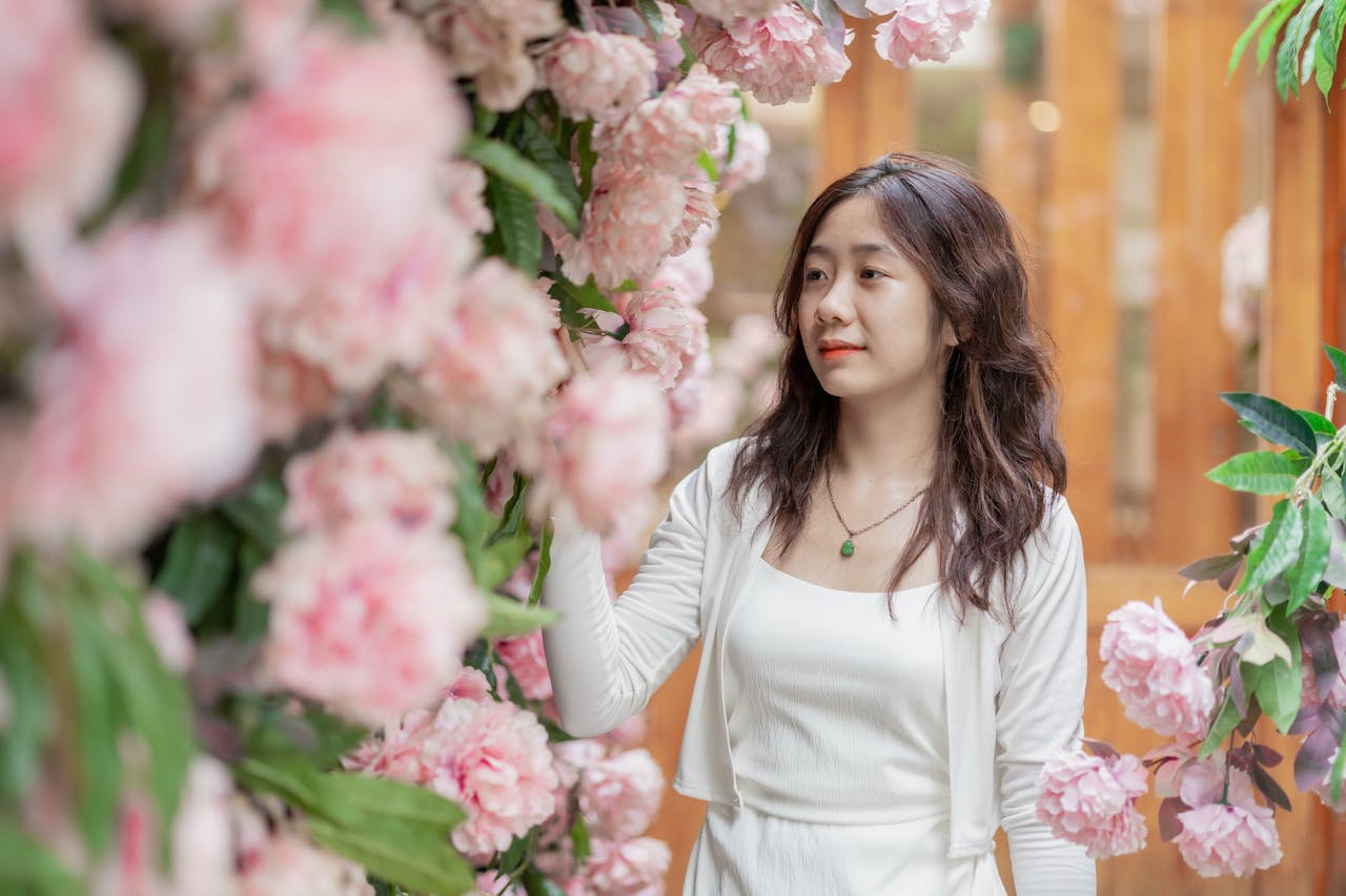 A woman in white gently touches blooming pink flowers, evoking tranquility and elegance.
